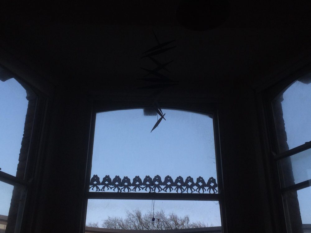 A backlit window showing a repeating paper chain design displayed on the sash window frame