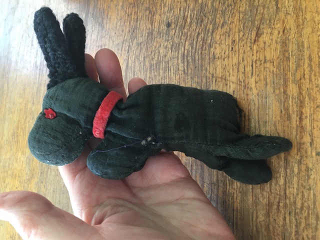 A hand holding an antique small black dog toy