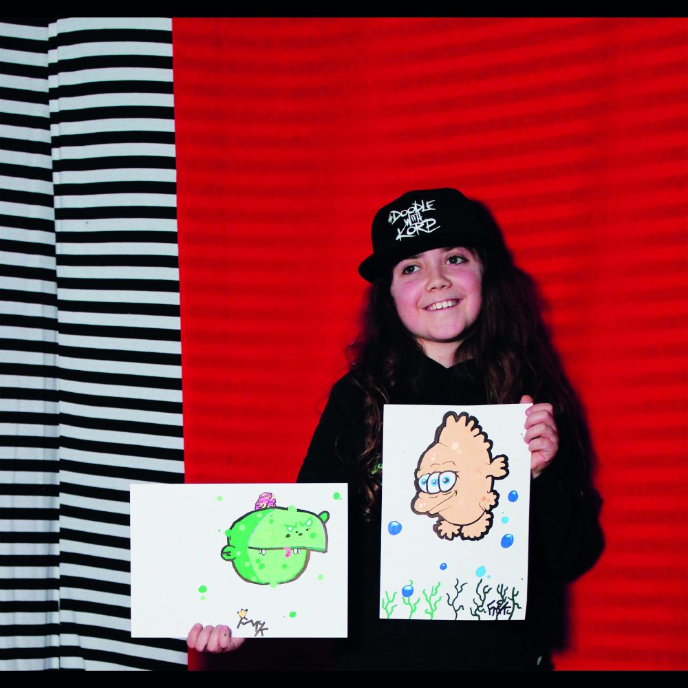 Child holding artwork in front of a red and black & white stripe background