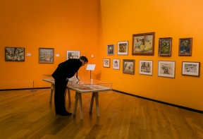 A person leans over a vitrine to view articles in the Denis Wirth Miller, Landscapes and Beasts Exhibition at Firstsite 2022.