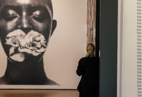 A woman in a black suit , leaning against a wall, observing the 'I Can't Breathe' artwork by EVEWRIGHT.