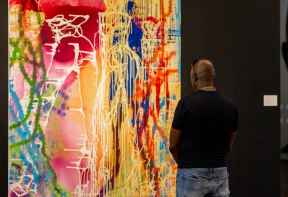 A man looking at one of the works from the Zoom Muses Series by EVEWRIGTH. It's a large-scale mixed media painting exploring a bold use of colour and a variety of painting techniques.