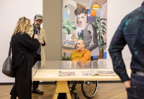 Three people (one in a wheelchair) having a discussion over an art piece at David Lock Exhibition.