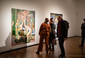 Two people looking at artist Jessie Makinson's large painting on an illuminated white wall.