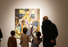 Three children and a man in the centre of the image looking at artist Jessie Makinson's large painting in front of them displayed on an illuminated white wall.