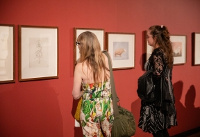 Two women in in colourful outfits looking at Leonora Carrington drawings at the Leonora Carrington: Avatars & Alliances exhibition