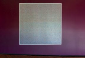 A square printed artwork on a burgundy wall showing a pixelated pattern.