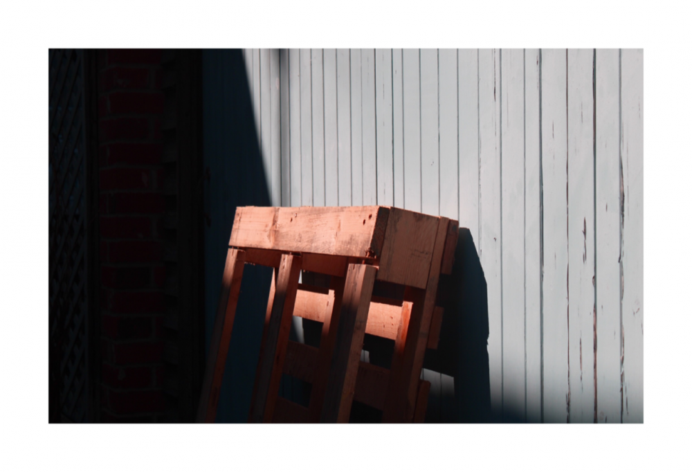 A close up of a pallet cleaning against a wall outside, half covered in shadow, the top half drenched with sunlight.