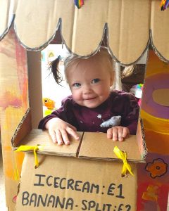 toddler playing in a homemade ice cream shop made from a cardboard box