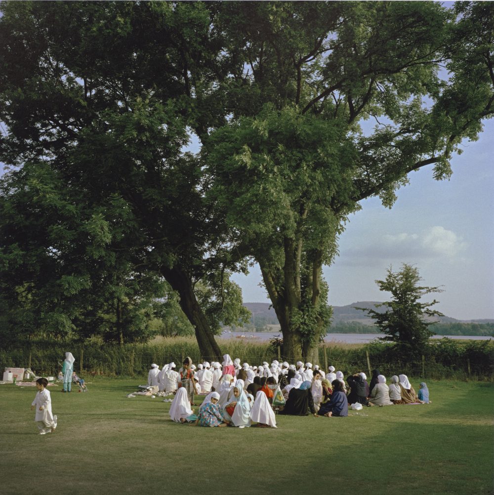 people gather for prayer on grass under a large tree in Windermere