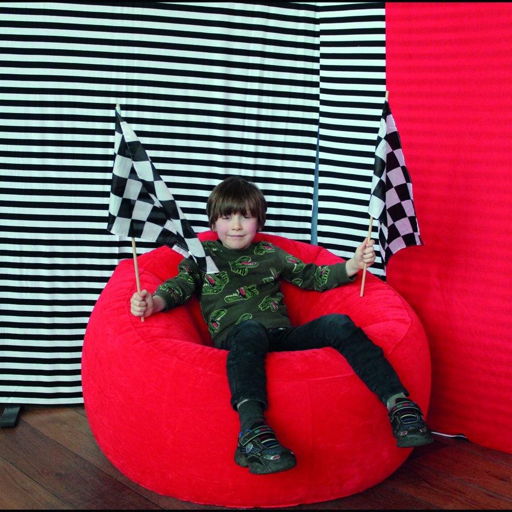 A child sitting on a red bean bag holding up two black and white checkered flags in front of a black & white stripe background.