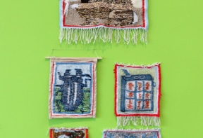 Colorful woven tapestries depicting various scenes, hung against a vibrant green wall.