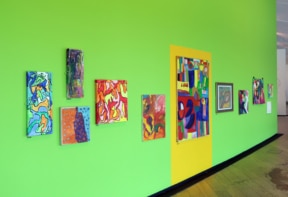 A vibrant green wall showcases colourful abstract artworks, with a bright yellow section containing an additional piece.