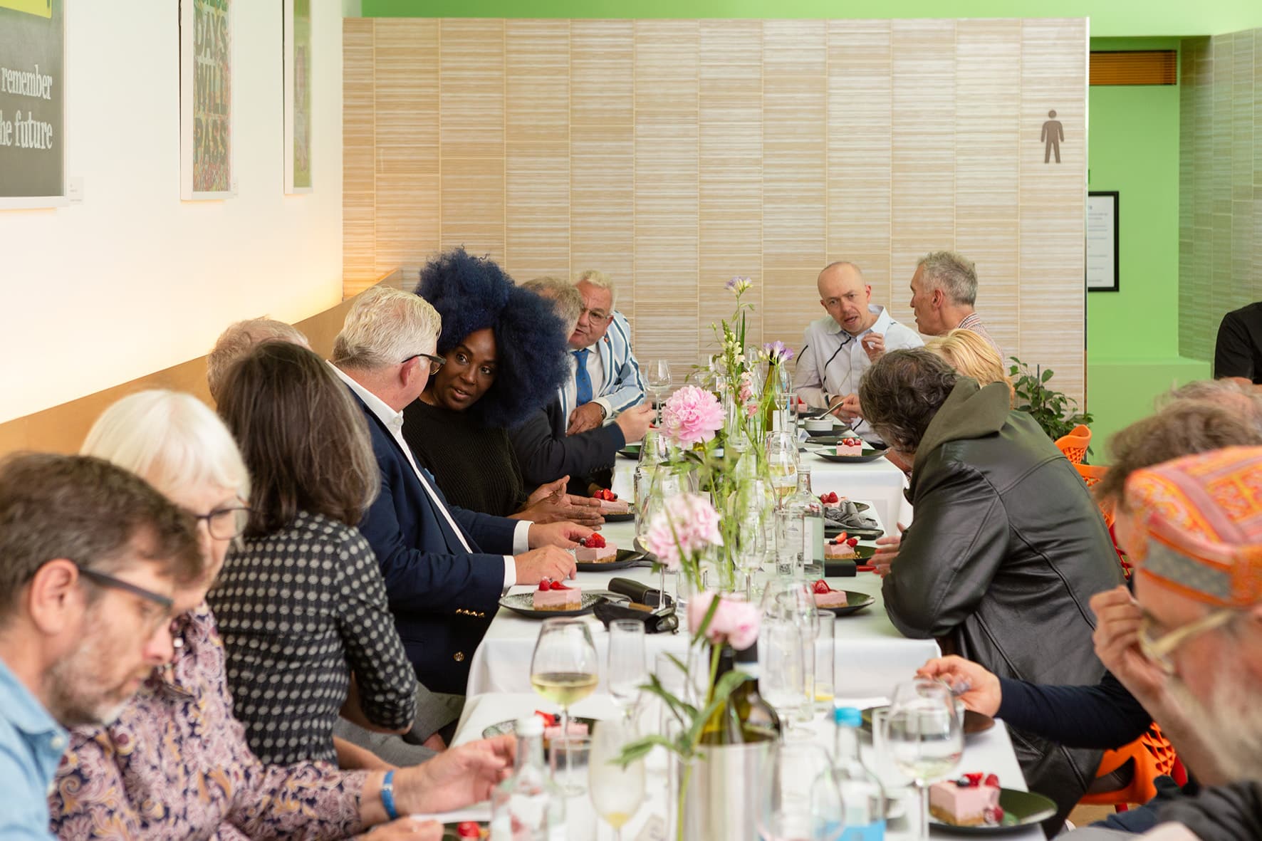 People sitting around a long rectangle table with a white cloth and flowers, food and drinks on top at the Berryfield Cafe.